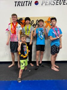 Five boys posing for a group photo wearing leis in front of a 'Truth Perseveres' banner at a youth camp.
