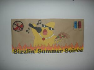 Colorful poster advertising a 'Sizzlin' Summer Soiree' with a cheerful yellow cartoon character wearing sunglasses, flames at the bottom, and small blue/red game controllers on the right side.